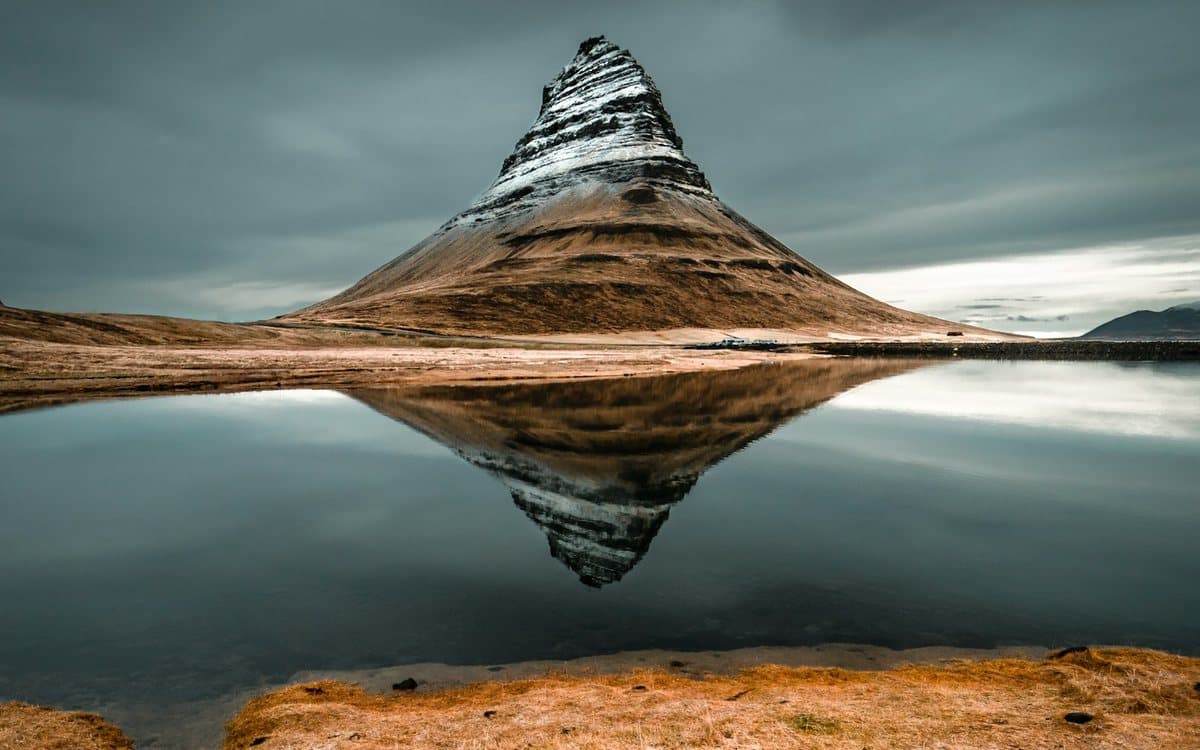 Kirkjufell's cone mirrored in still water above golden grass